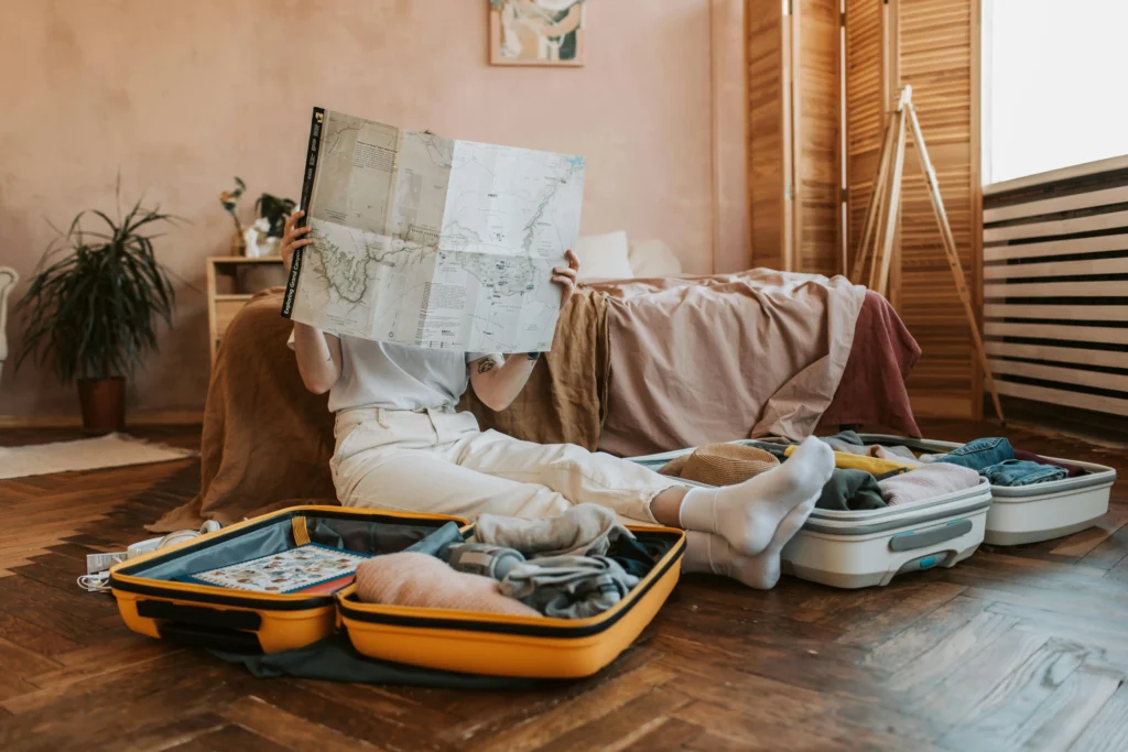 woman holding a map in front of her face surrounded by open suitcases full of clothes